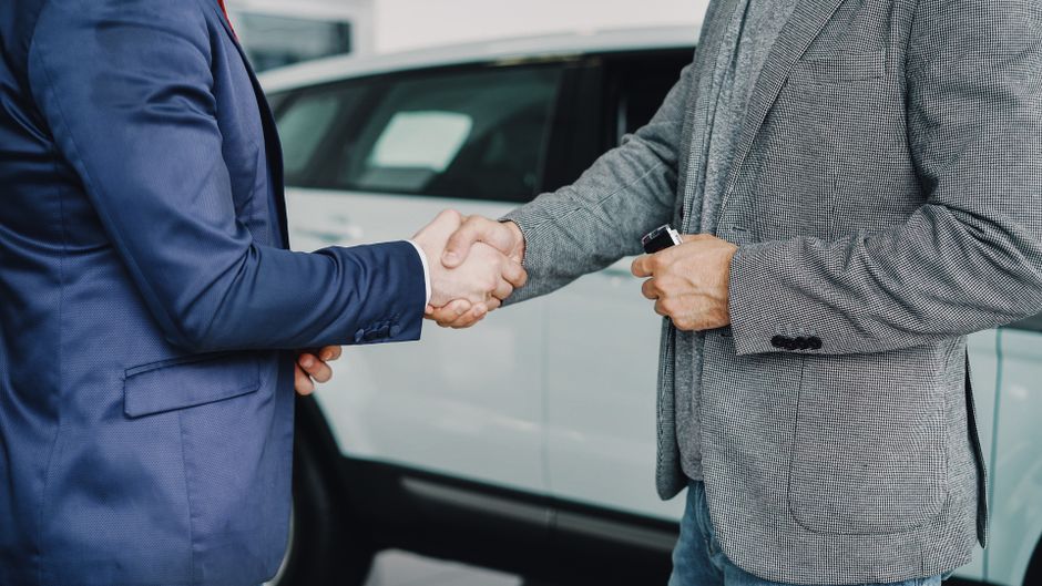 Dvojica poslovnih ljudi rukuju se u salonu automobila nakon dogovora